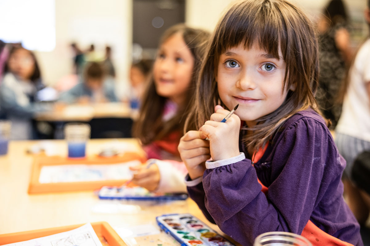 child in purple shirt sitting at a table with watercolors